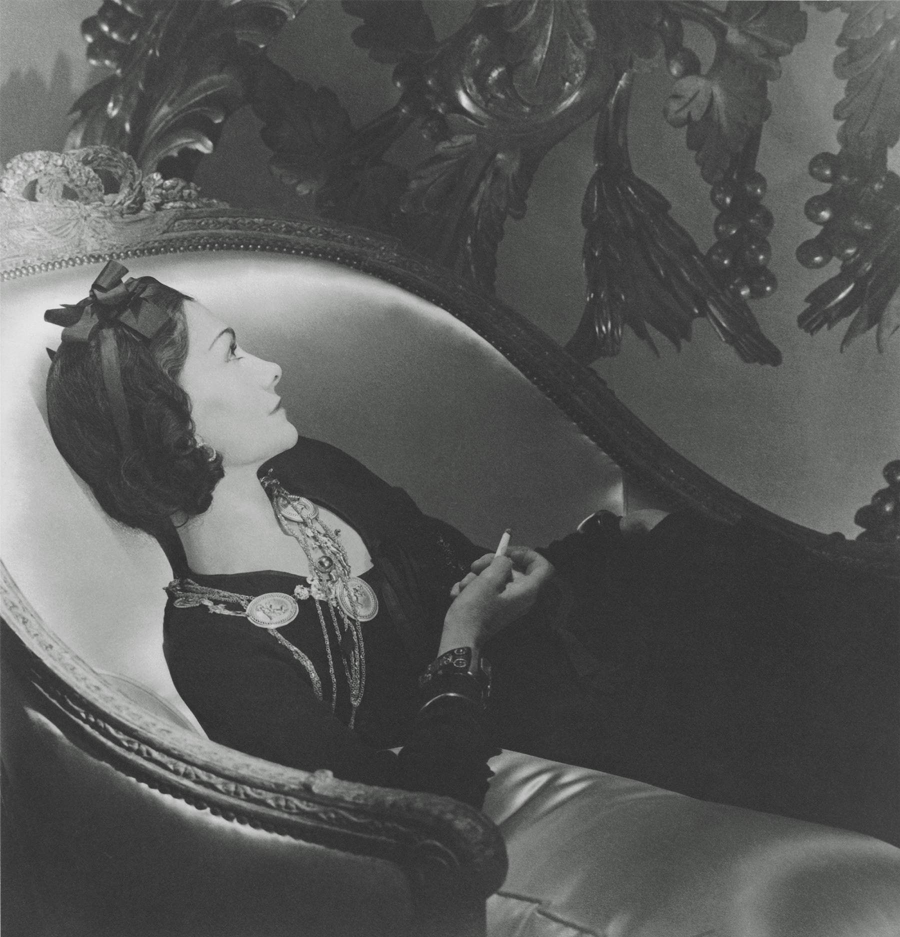 1937, Paris, France --- French fashion designer Coco Channel, in profile reclining on a chaise lounge with cigarette, wearing a dark dress with gold medallion necklaces and a ribbon in her hair; photographed in Paris in 1937. --- Image by Æ Cond⁄ Nast Archive/CORBIS